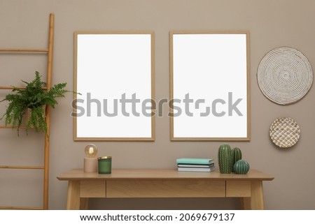 Empty frames hanging on beige wall over wooden table with decor. Mockup for design