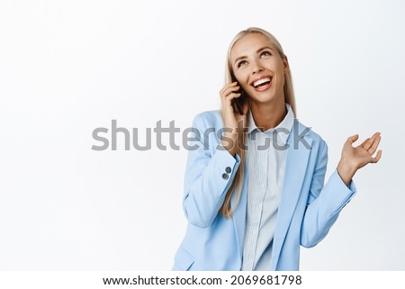 Talkative cute businesswoman talking on mobile phone, smiling and having happy conversation, standing over white background