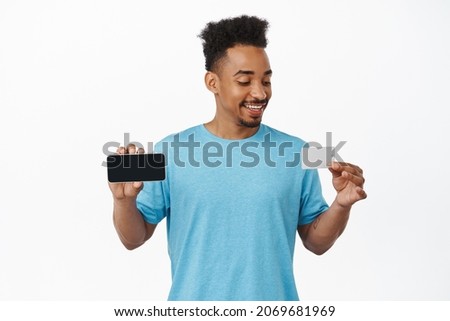 Handsome african american male model, showing smartphone horizontally, credit card, smiling satisfied, recommend payment method, purchase online, white background