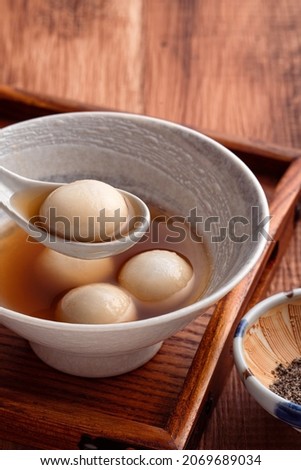 Close up of sesame big tangyuan (tang yuan, glutinous rice dumpling balls) with sweet syrup soup in a bowl on wooden table background for Winter solstice festival food. Royalty-Free Stock Photo #2069689034