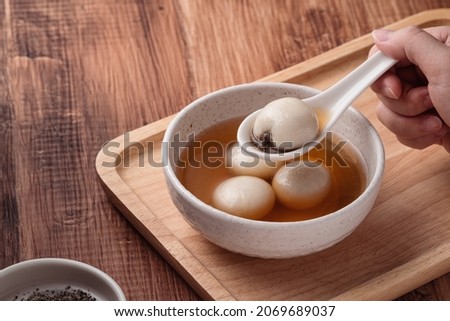 Close up of sesame big tangyuan (tang yuan, glutinous rice dumpling balls) with sweet syrup soup in a bowl on wooden table background for Winter solstice festival food. Royalty-Free Stock Photo #2069689037