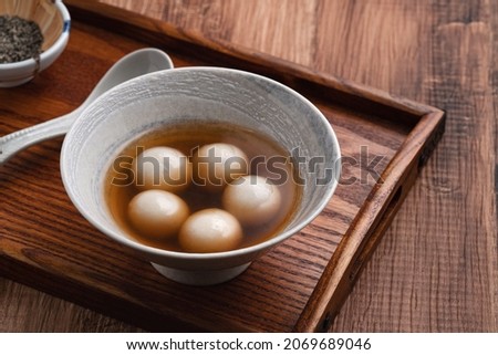 Close up of sesame big tangyuan (tang yuan, glutinous rice dumpling balls) with sweet syrup soup in a bowl on wooden table background for Winter solstice festival food. Royalty-Free Stock Photo #2069689046