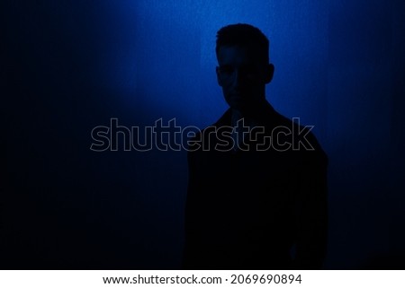 male silhouette on a blue background, the face is almost invisible. portrait to the waist.