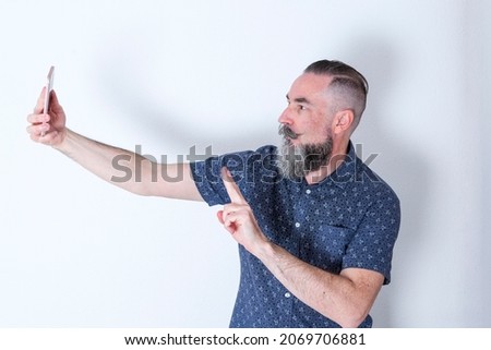  bearded hipster man in his 40s taking a selfie of himself with his fingers pointing to the victory sign