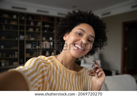 Happy young African American multiracial woman holding keys in hands, recording selfie video or posing for photo, feeling excited of purchasing own apartment or renting first dwelling, real estate.