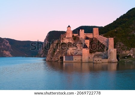 Aerial, view across the water of medieval fortress Golubac, standing on the banks of the Danube river. Fortress towers illuminated by pink light.  Aerial photo. Traveling concept background. Serbia.  Royalty-Free Stock Photo #2069722778