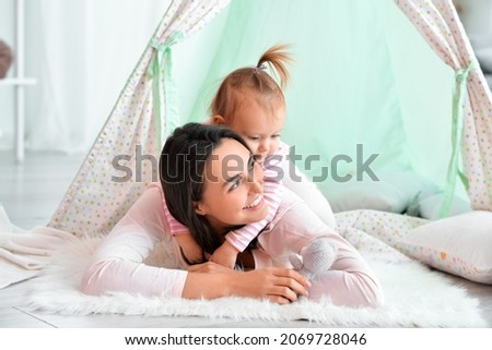Happy woman and her little daughter playing in wigwam at home