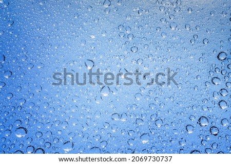 Blue water droplets and raindrops cling to the cool clear glass.
