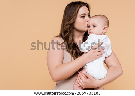 Plus size mother kissing baby daughter isolated on beige