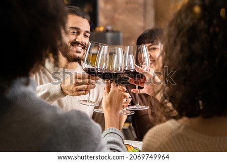 Friends toasting red wine - Young people clinking sitting at the restaurant table - blurred faces - focus on the wineglasses