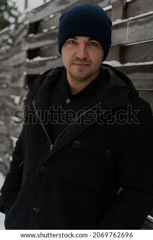 business man portrait near wooden stylish fence. in a hat, coat handsome on a winter walk in the forest before christmas