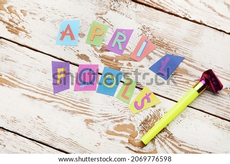 Party horn and text APRIL FOOLS on white wooden background