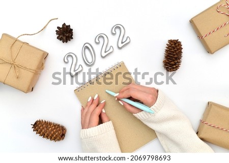 New year decoration. Writing of 2022. Woman hands are writing on the craft papper. Top view. Wite background.