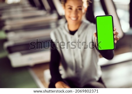 Close-up of sportswoman showing screen of her mobile phone during sports training in a gym. Copy space.