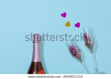 Champagne bottle with two glasses filled with confetti lying on blue paper background. Valentine's Day celebration celebration. Copy space for ad. Concept of holidays, celebrations, greeting. Faceless