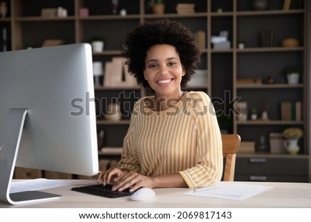 Portrait of happy attractive young African American businesswoman freelance worker employee looking at camera, sitting at table with computer, posing in modern home office, career concept. Royalty-Free Stock Photo #2069817143