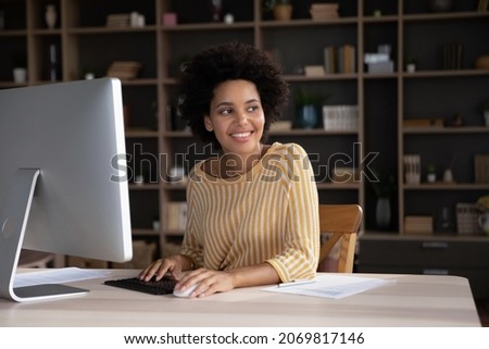Thoughtful smiling young African American business lady working on computer in modern home office, looking in distance considering project problem solution or creating new ideas, feeling motivated.