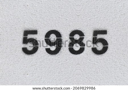 Black Number 5985 on the white wall. Spray paint. Number five thousand nine hundred and eighty five.