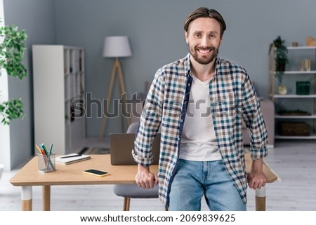 Photo of confident handsome young man wear plaid shirt smiling sitting table smiling indoors house office