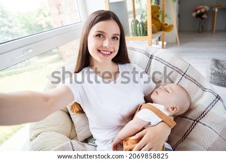 Photo of cheerful positive charming mother take selfie hold cuddle baby kid sleep wear white t-shirt home indoors Royalty-Free Stock Photo #2069858825