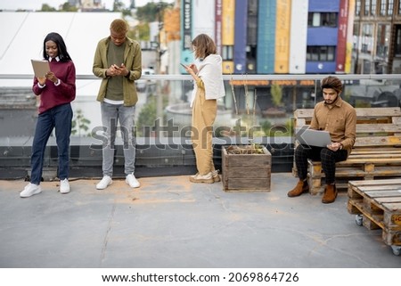 Focused multiracial students using digital devices on balcony at university campus. Concept of education. Remote and e-learning. Idea of student lifestyle. Persons wearing casual clothes
