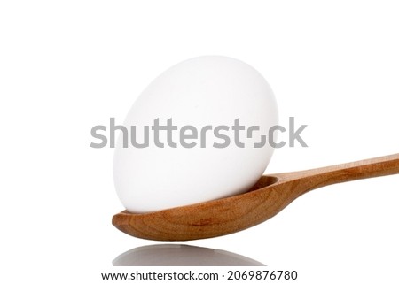 One white chicken egg with a wooden spoon, close-up, isolated on white.