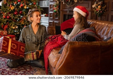Happy family portrait. A picture of mother and daughter in Santa hat with wrapped presents in Christmas decorated living room. 