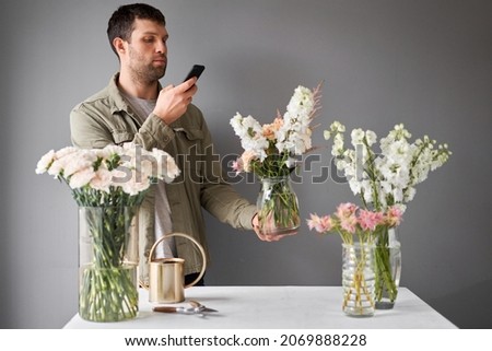 Male florist with a mobile phone, takes a photo to confirm the order. Accepts an online order for flower delivery. Responds to messages in social networks and online messengers.