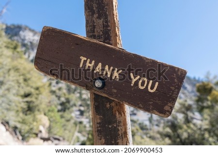 Rustic wooden thank you sign with mountain wilderness background.