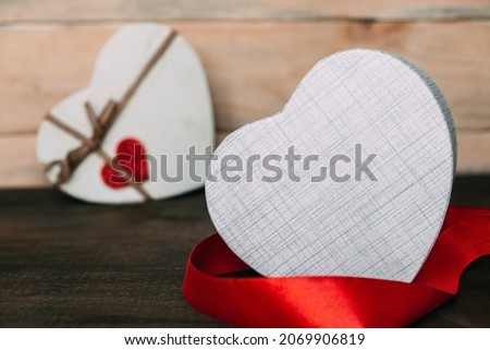 Heart-shaped box is surrounded by a red ribbon. Two gift boxes on a wooden background. Valentine's Day.