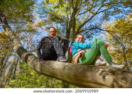 Father and daughter climbed on tree. Family sitting in a tree in an autumn forest