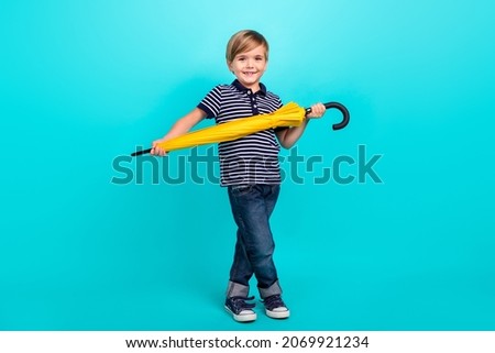Full body photo of nice little boy hold umbrella wear t-shirt jeans sneakers isolated on teal background