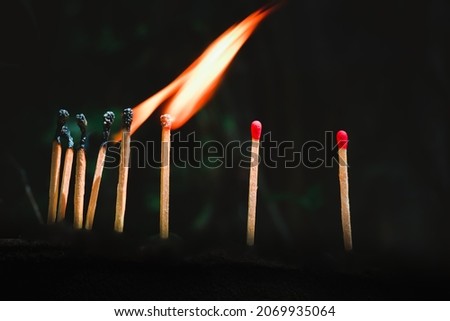 The concept image of burning matches igniting other matchsticks in a row against a black background.  Royalty-Free Stock Photo #2069935064
