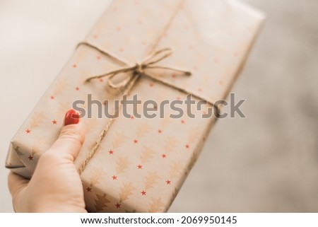 Christmas time is about giving gifts. A woman with red nail polish  is giving a present wrapped in brown paper with christmas trees and twine.