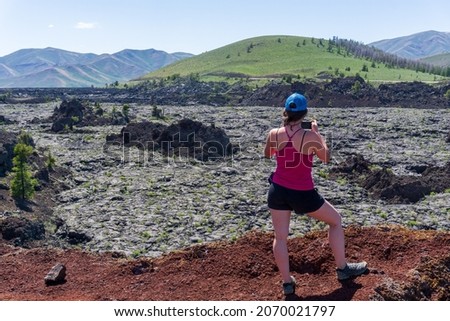 Woman hiker taking pictures of black and green volcanic landscape at Craters of the Moon National Monument in Idaho USA