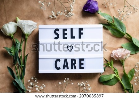Self-care word on lightbox and flowers on color background flat lay. Take care of yourself