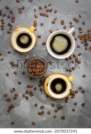 There are three cups on a wooden round stand, in which there is black coffee with sugar, there are a lot of coffee beans nearby