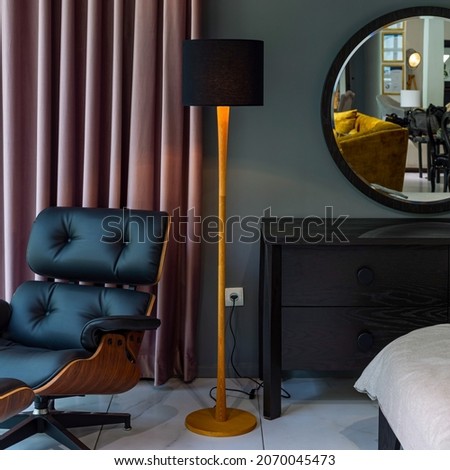 A lampshade in a room with relaxing chair, curtain, drawer and a mirror.