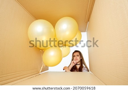 Beautiful happy girl opens a gift box with balloons