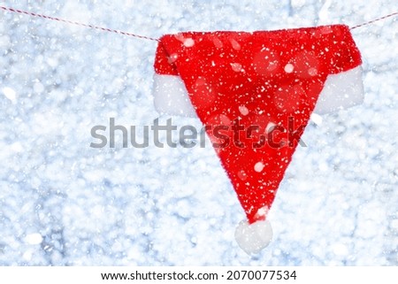 A red Christmas cap hangs on a rope. Against the backdrop of a blurred shiny white-blue background. Concept. Template for design. Copy space