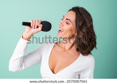 Young woman in a white evening dress on a light green background with bright pink makeup holds a microphone, sings karaoke