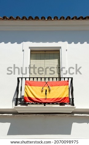 Flag of Spain with a black ribbon for mourning  on the balcony of a whitewashed house in Andalusia town