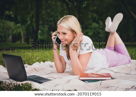 Full size profile photo of aged cute blond lady sit talk telephone laptop wear t-shirt trousers sneakers in park alone