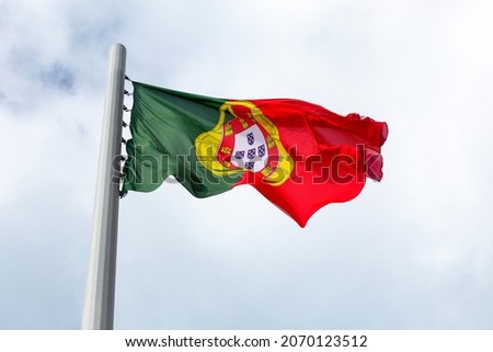 A large flag of Portugal is flying in a strong wind in a cloudy sky
