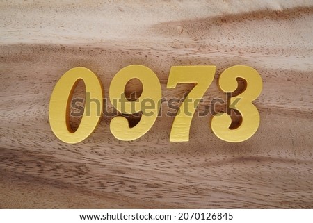 Golden Arabic numerals 0973 on a dark brown to white wood grain background.