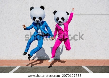 Storytelling image of a couple wearing giant panda head and colored suits. Man and woman making party in a parking lot. Royalty-Free Stock Photo #2070129755