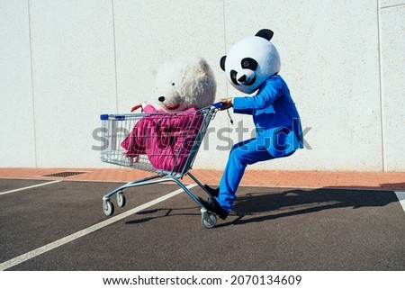Storytelling image of a couple wearing giant panda head and colored suits. Man and woman making party in a parking lot. Royalty-Free Stock Photo #2070134609