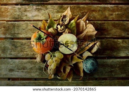 Still life, top view of: dry leaves, grapes, walnuts, persimmons and pewter container with incense stick on wooden slatted table. Antique effect.
