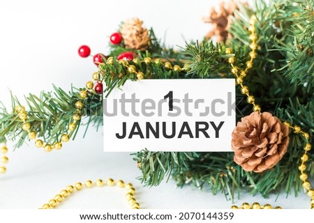 1 January text on a card on a spruce branch with a Christmas decoration on a white background