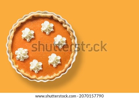 Homemade Traditional American Pumpkin Pie with whipped cream for Thanksgiving Day isolated on orange background. View from above. Copy space.